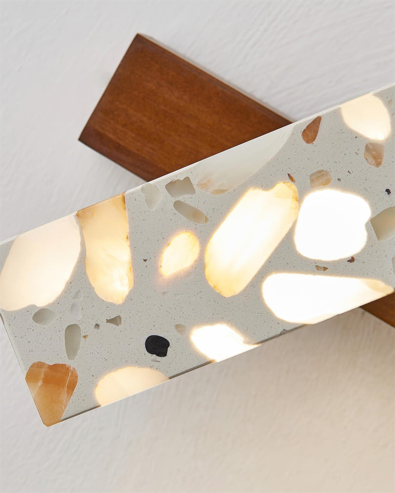 Close-up of the terrazzo wall sconce PIETRA No.07 lit, walnut base and backlit chips seen from below
