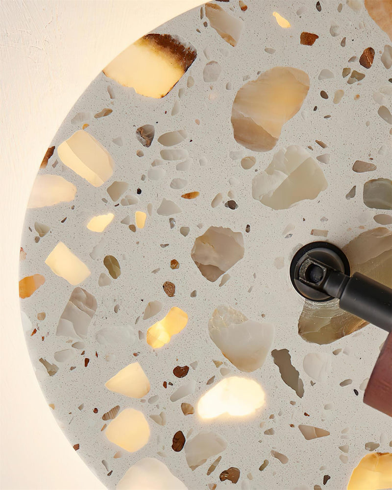 Close-up of the backlit terrazzo disc of the PIETRA No.08 wall sconce, stone chips glowing around the pivot