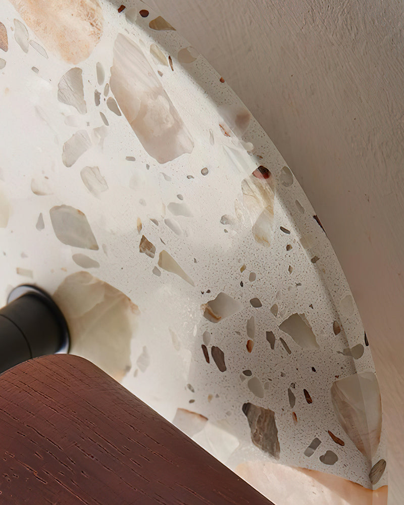 Close-up of the terrazzo wall sconce PIETRA No.08 showing the speckled stone plate edge and walnut cylinder