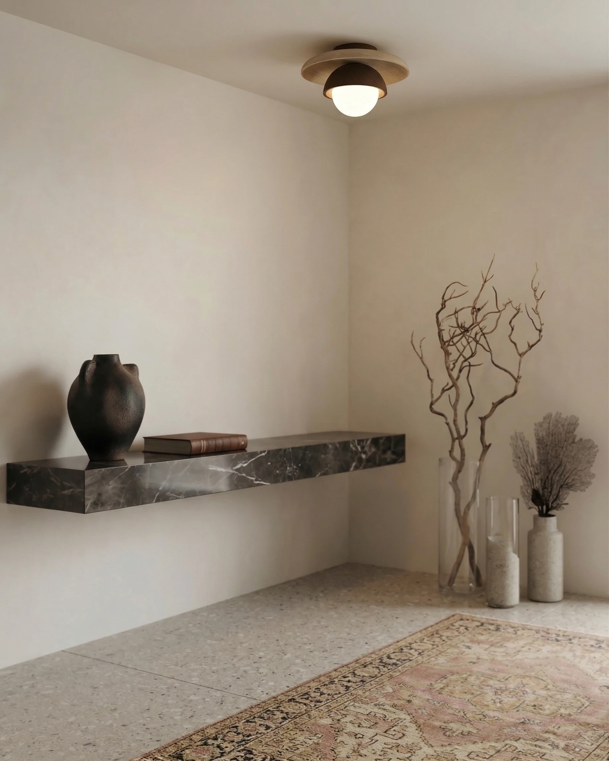 Travertine flush mount ceiling light LUNA No.03 lit above a floating black marble shelf with a vase and dried branches