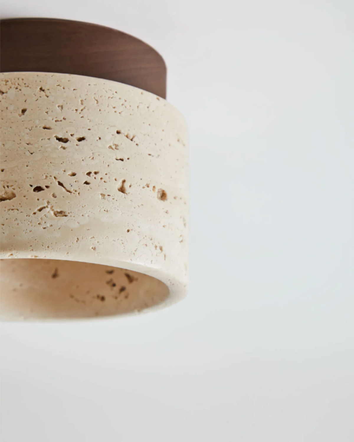 Close-up of the travertine flush mount ceiling light VERTIN No.05 in cream, showing the pitted stone drum and walnut cap
