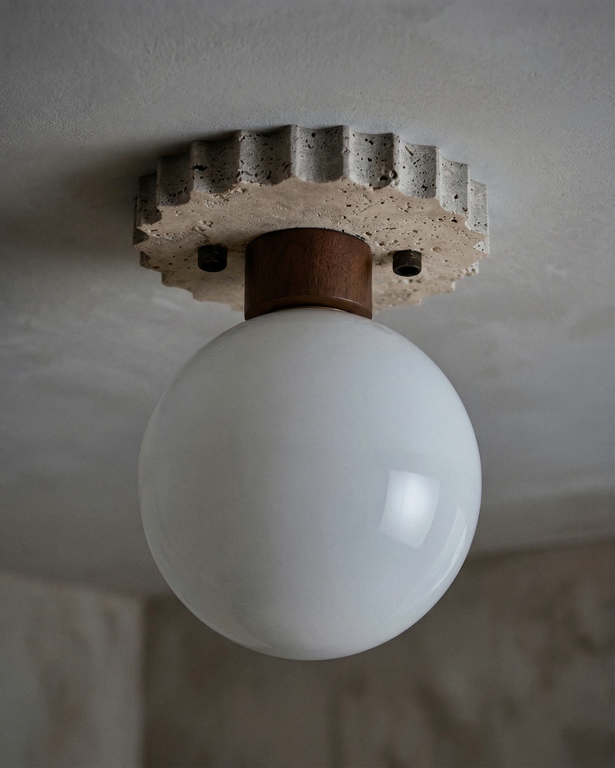 Close-up of the LUNA No.07 travertine flush mount ceiling light unlit, white globe under the walnut collar on a gray ceiling
