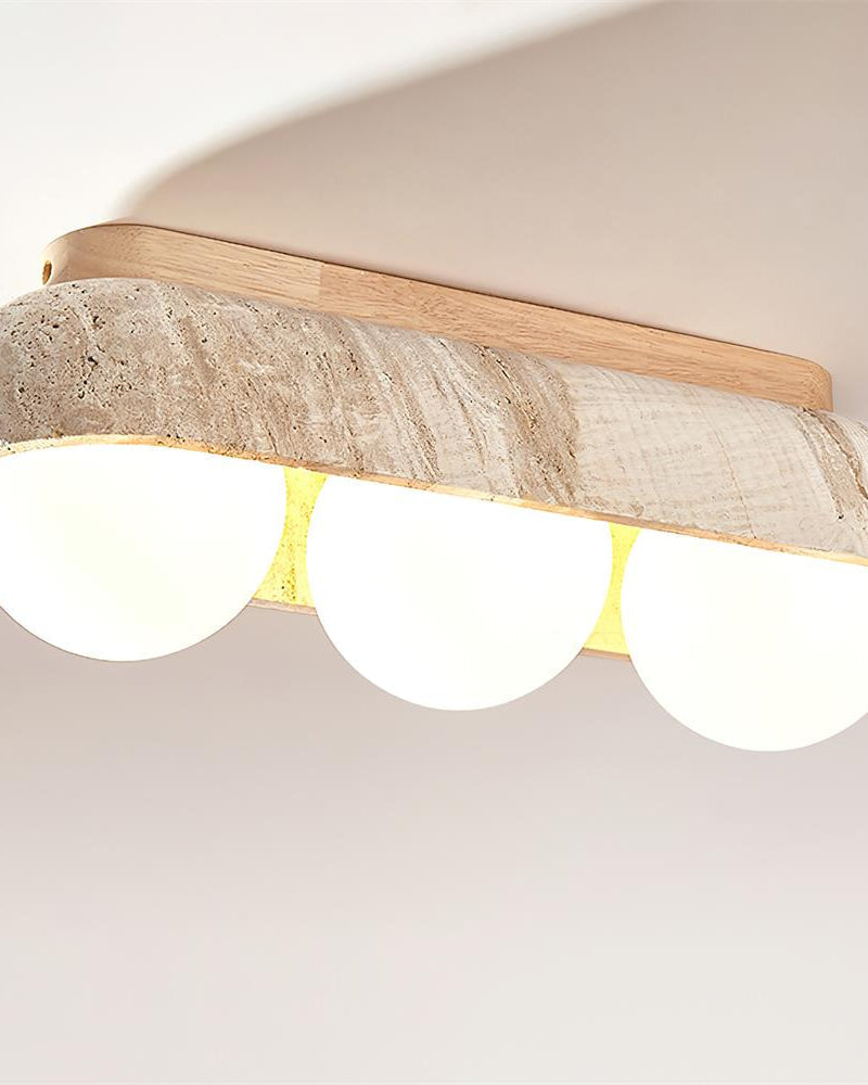 Close-up of the PIETRA No.03 travertine flush mount ceiling light, Three-Globe in Light Wood, all three globes switched on