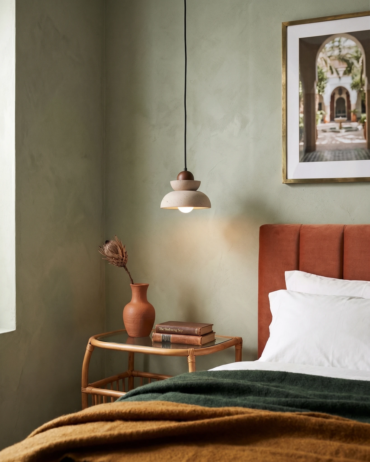 Travertine pendant light DOMUS No.02 lit beside a bed with a rust headboard and green bedding, walnut sphere on top