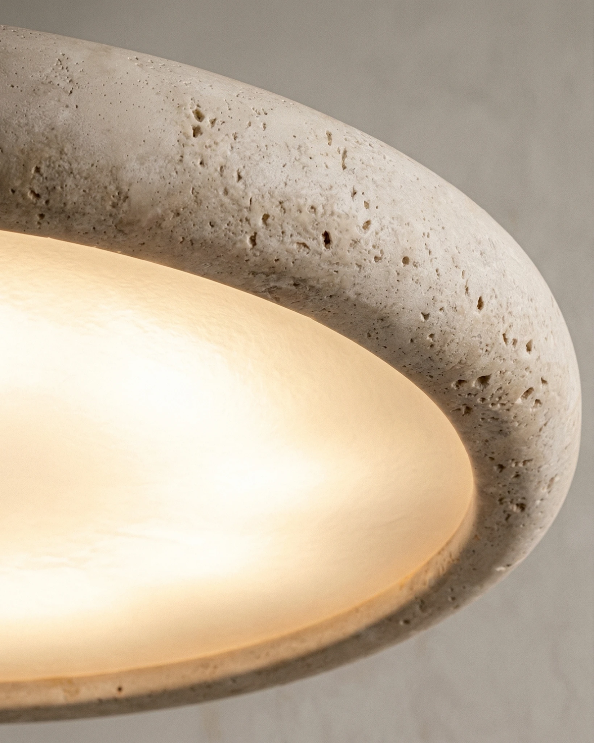 Close-up of the pitted travertine edge and glowing underside of the TONDO No.02 travertine pendant light