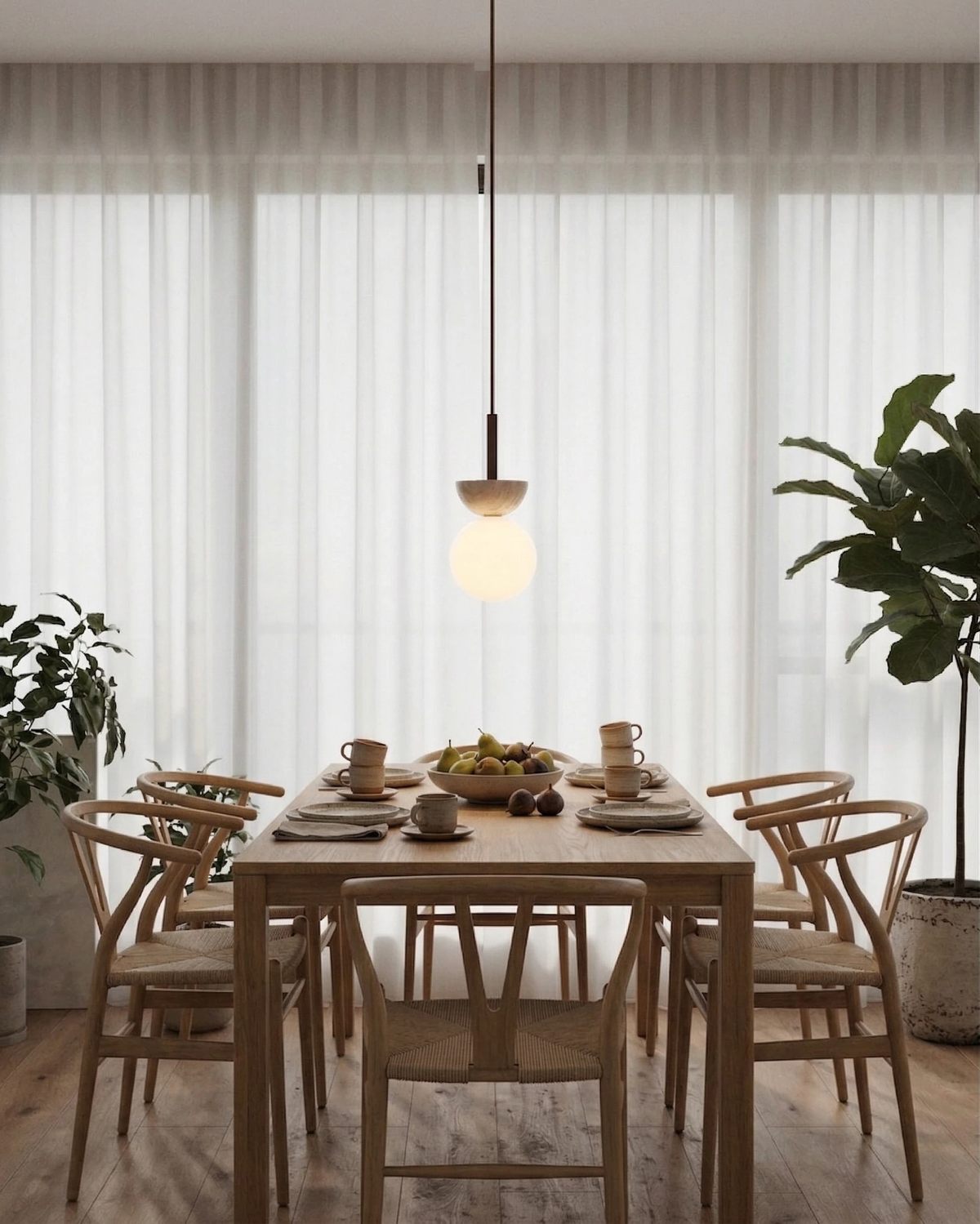 Travertine pendant light SOVA No.04 lit above a wooden dining table with wishbone chairs and sheer curtains