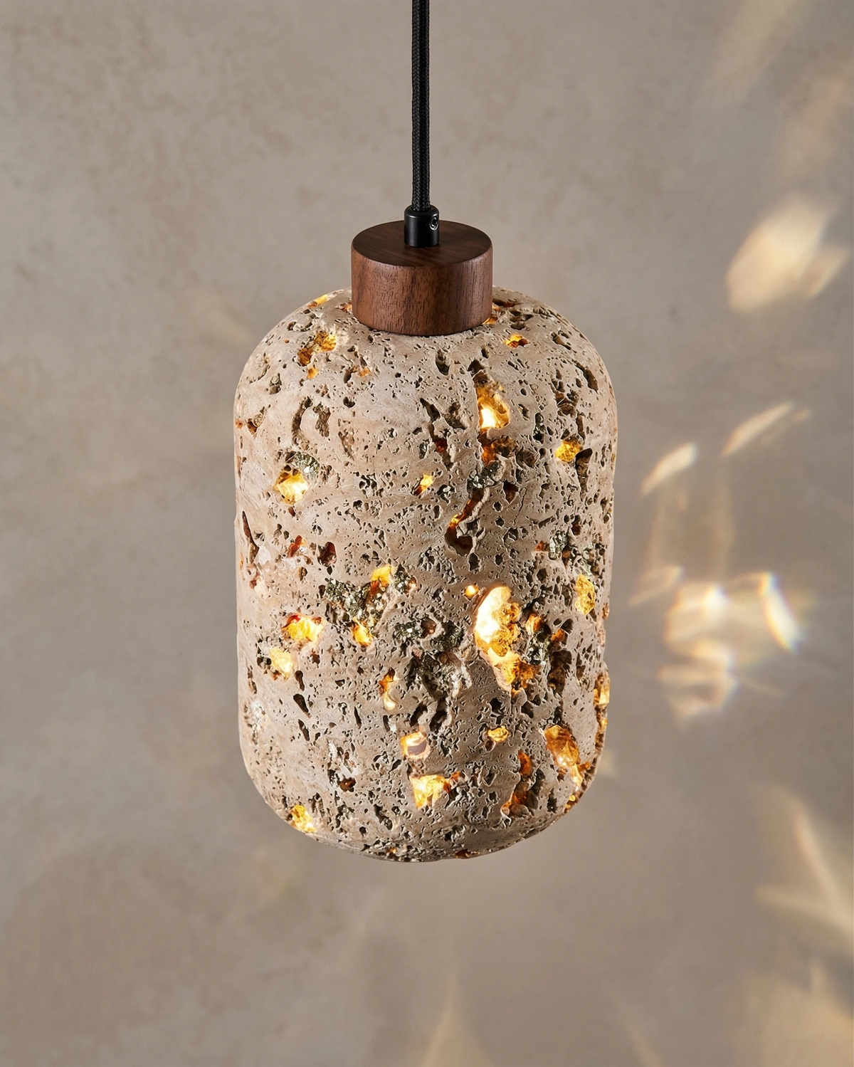 Travertine pendant light MASSA No.01 switched on, pored cylinder throwing dappled light onto a plaster wall