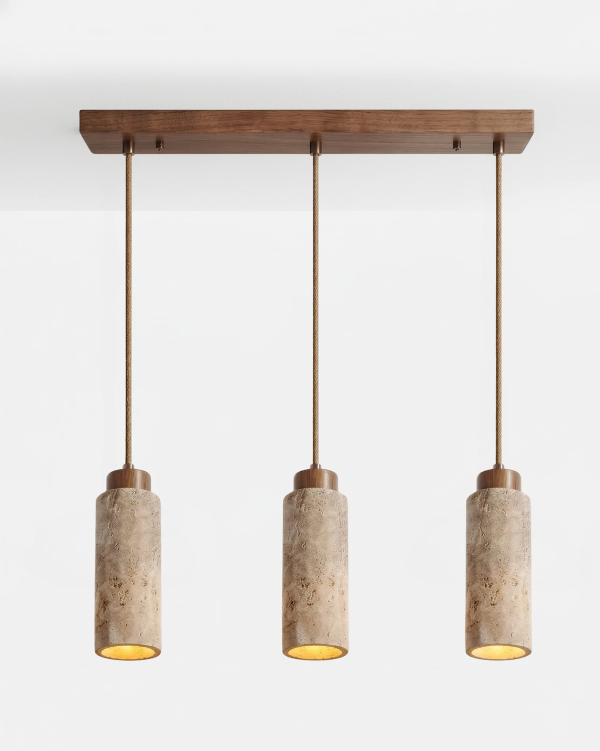 Travertine pendant light CORTO No.03 linear trio in cream, three cylinders in a row on a walnut bar canopy, switched on