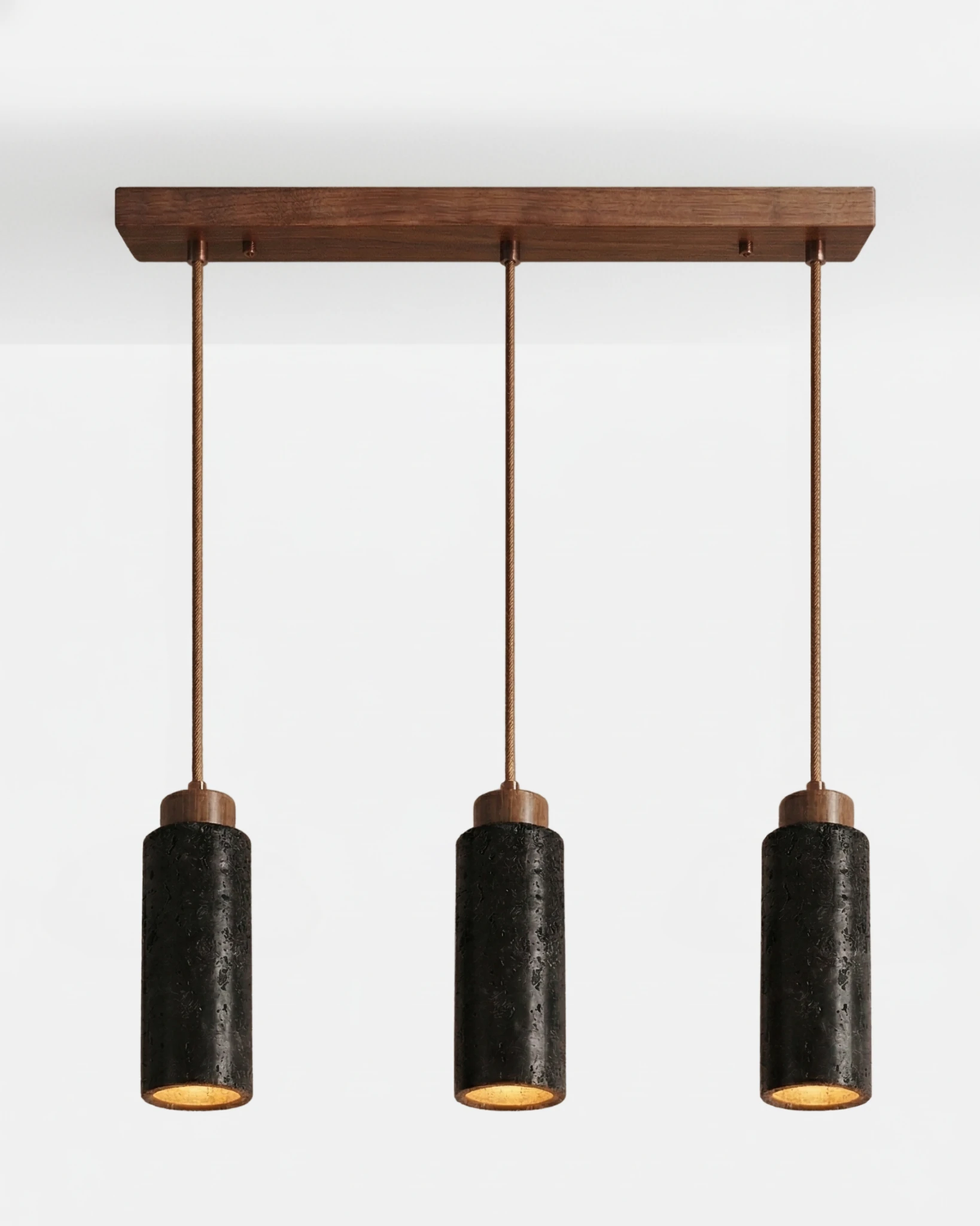 Travertine pendant light CORTO No.03 linear trio in Volcano Black, three dark cylinders on a straight walnut bar, lit