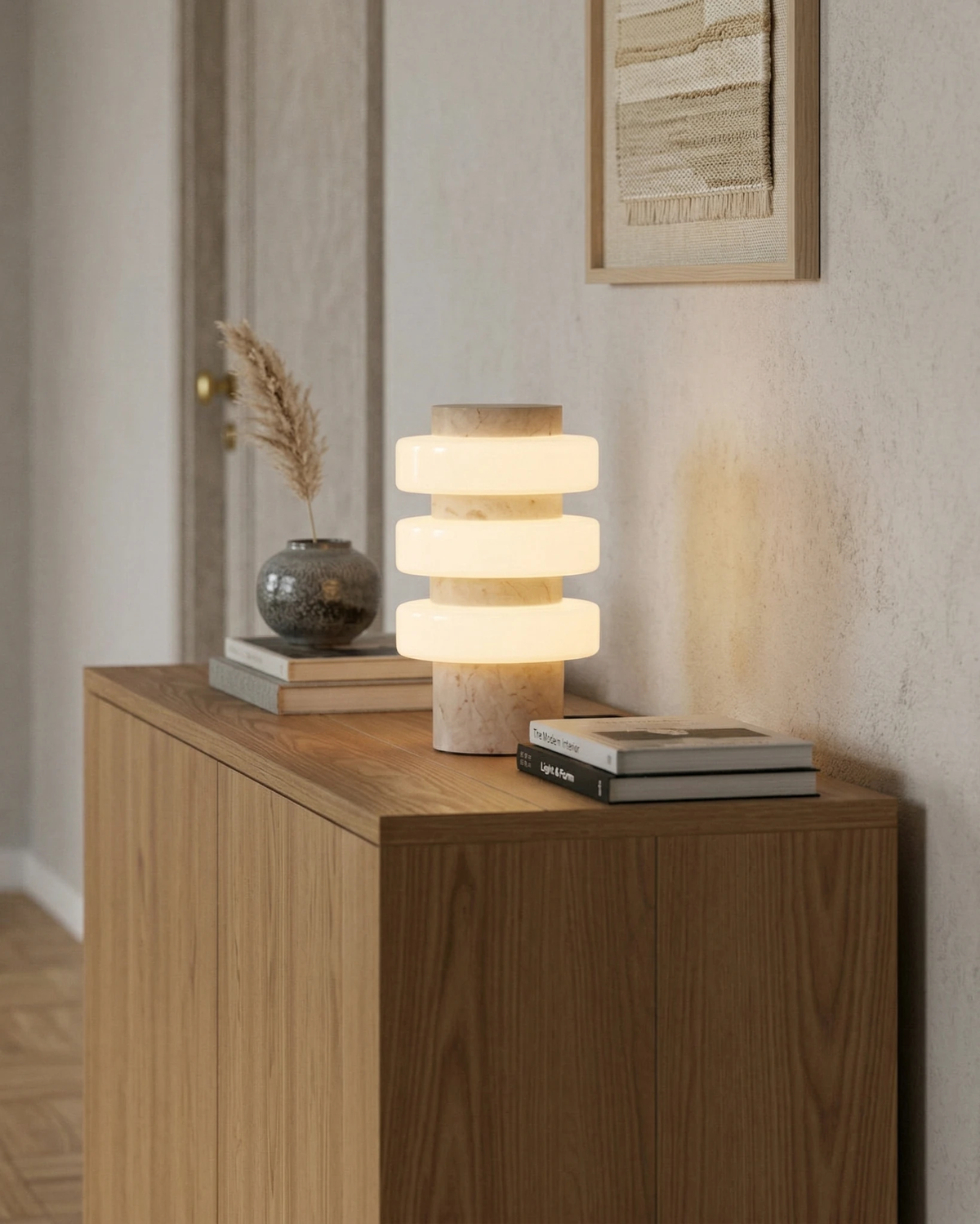 Travertine table lamp PIETRA No.05 switched on atop an oak cabinet with a small vase and books