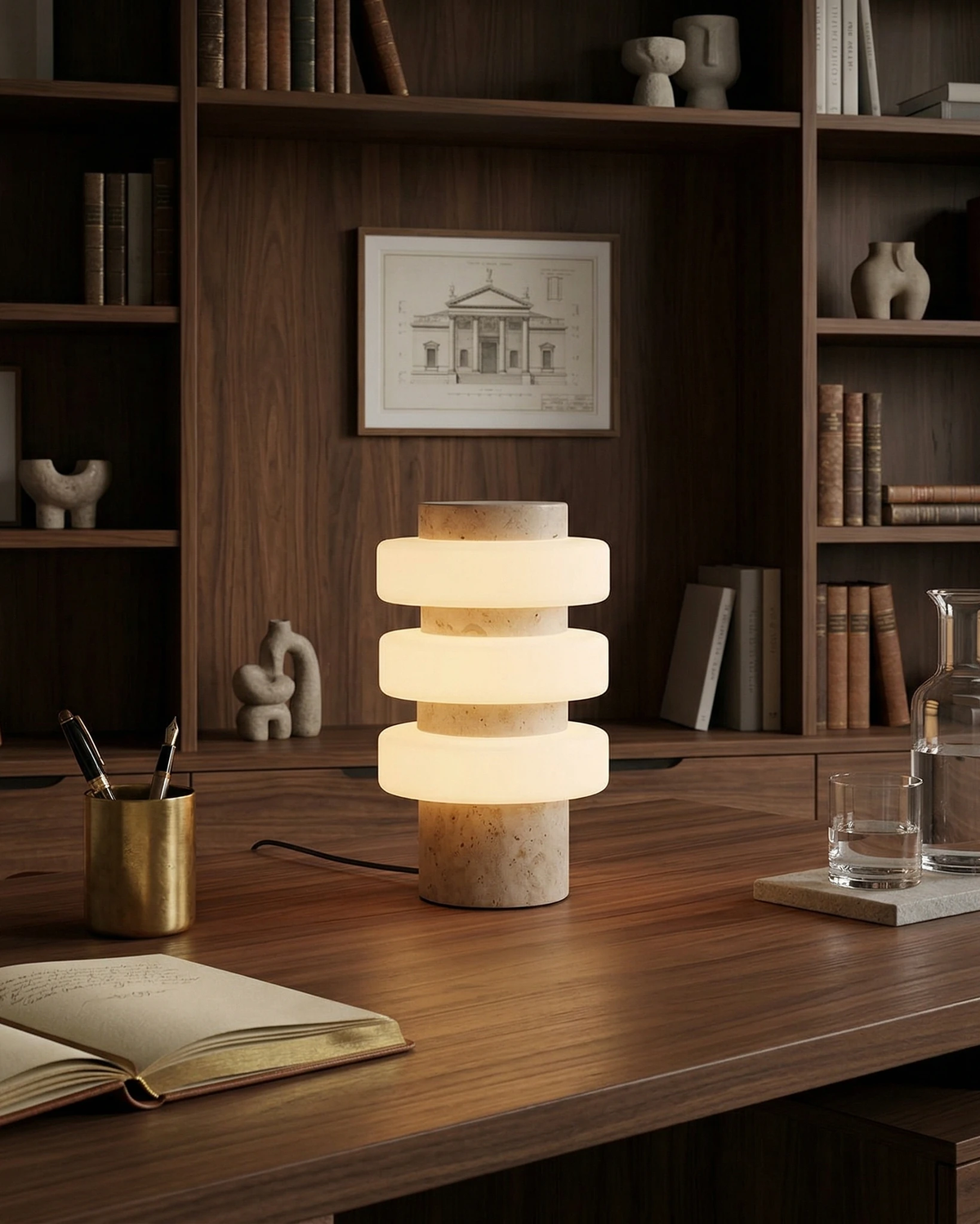 Travertine table lamp PIETRA No.05 in cream travertine lit on a walnut desk in front of bookshelves
