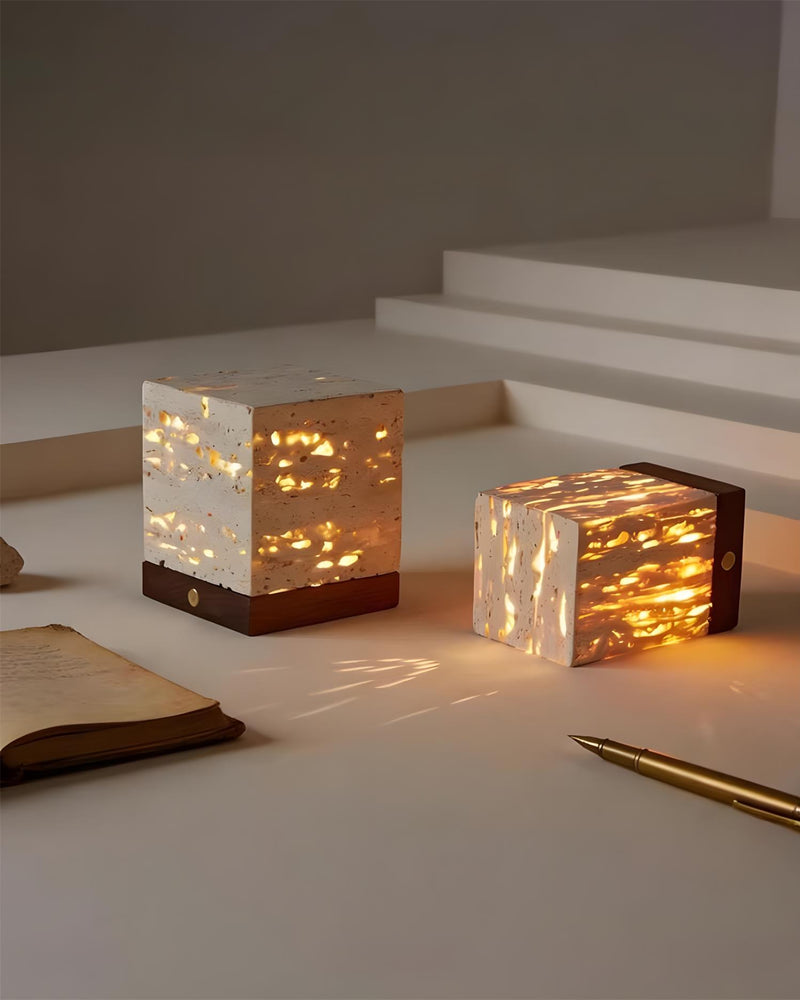 Two travertine table lamps MORA No.05 glowing on a white surface beside an open notebook and a gold pen