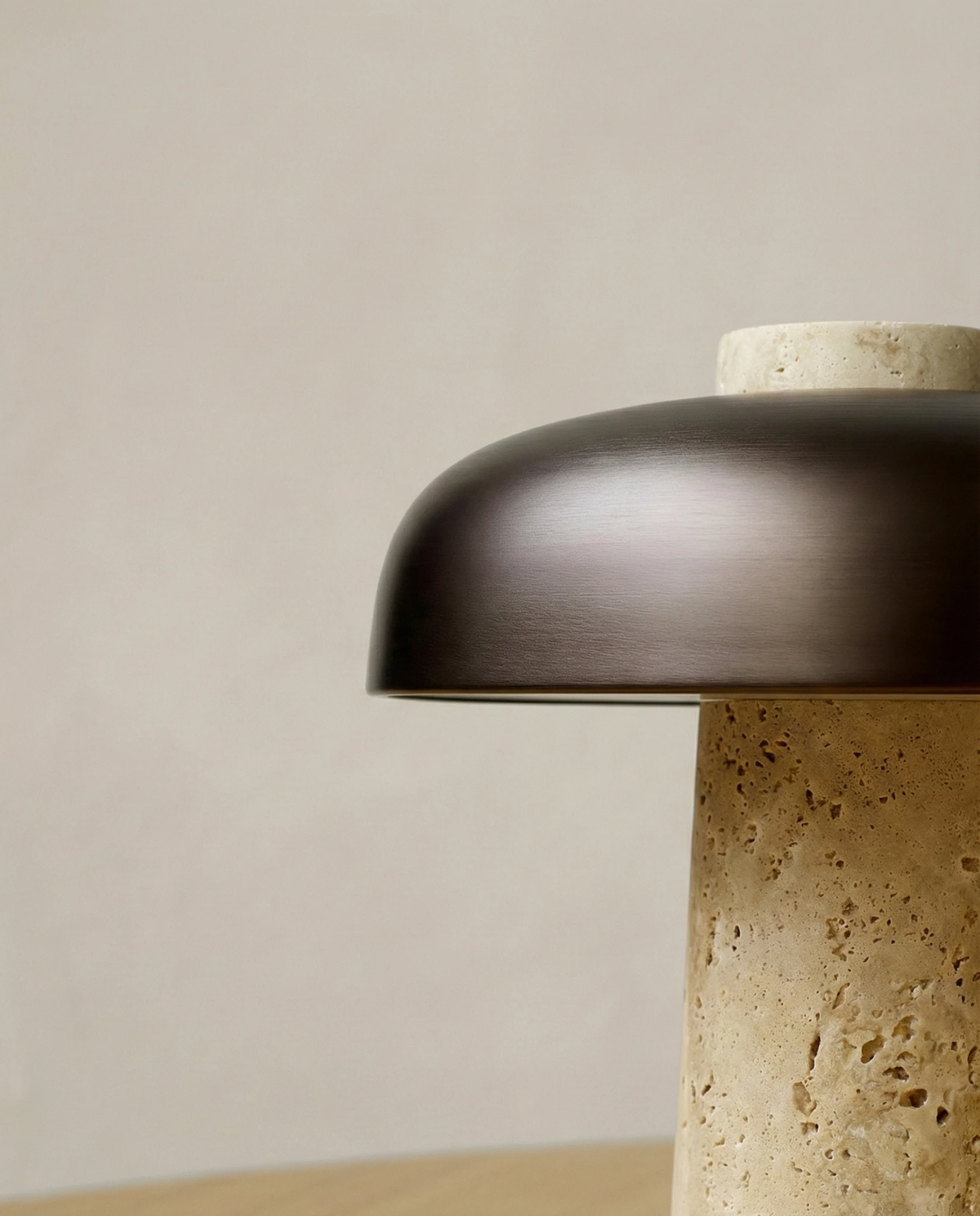 Close-up of the dark bronze dome and pitted travertine column of the travertine table lamp ROCCA No.03