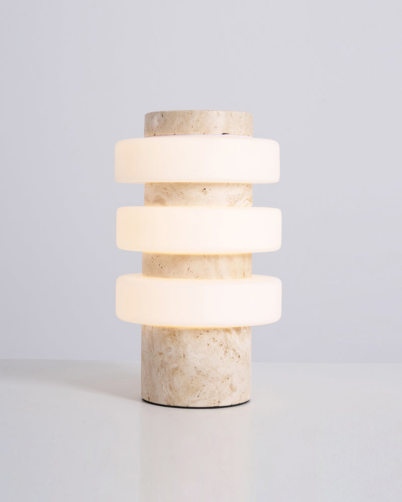 Travertine table lamp PIETRA No.05 in cream travertine switched on, acrylic rings glowing between stone tiers