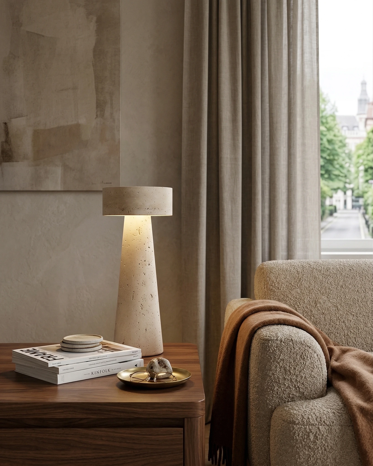 Travertine table lamp MORA No.02 lit on a wooden side table with books beside an armchair by a window