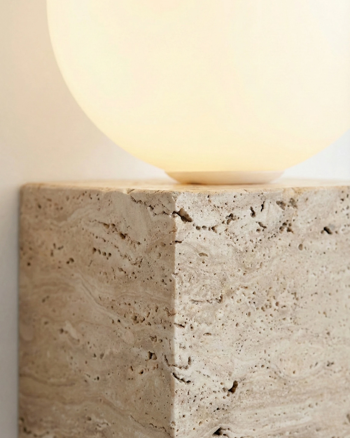 Close-up of the pitted travertine cube and lit opal globe of the MODENA No.01 travertine vanity light