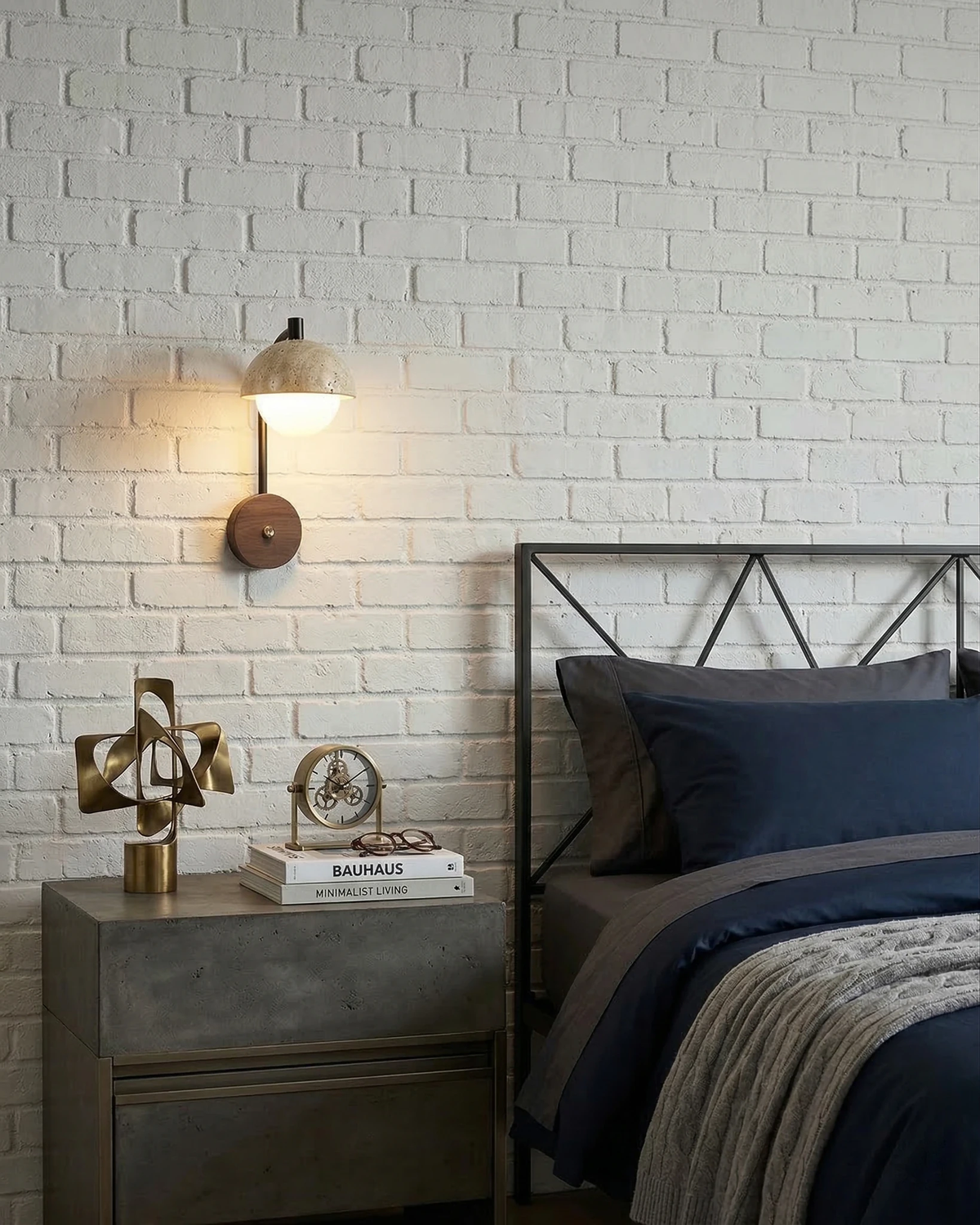 Travertine wall sconce AVORIO No.03 lit on a white brick wall above a nightstand beside a bed with navy bedding