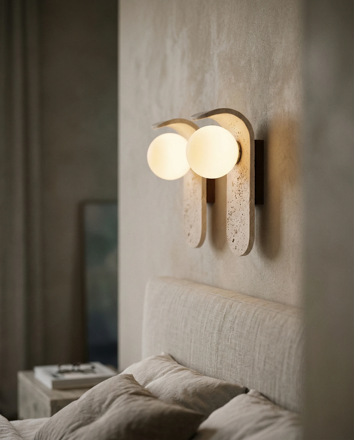 Travertine wall sconce ARCO No.01 switched on above a boucle headboard with a pillow and folded linen below