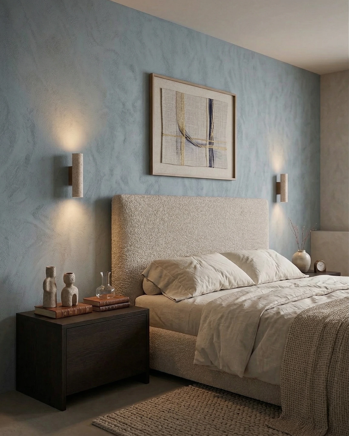 Pair of travertine wall sconces STELO No.02 lit on a blue wall flanking a bed with a cream headboard