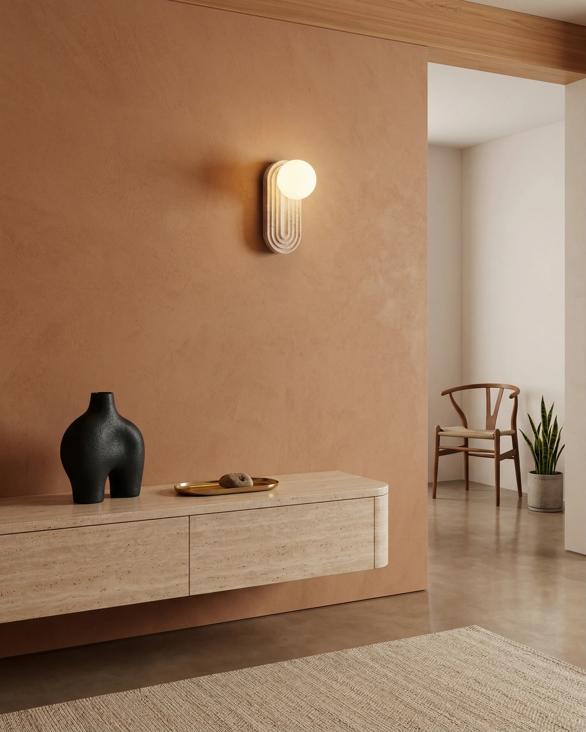 Travertine wall sconce ARCA No.01 lit on a terracotta wall above a floating oak console with a black vase