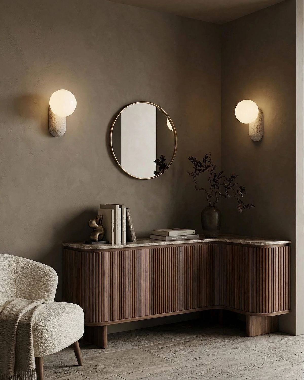 Two travertine wall sconces PERLA No.01 lit either side of a round mirror above a fluted walnut sideboard