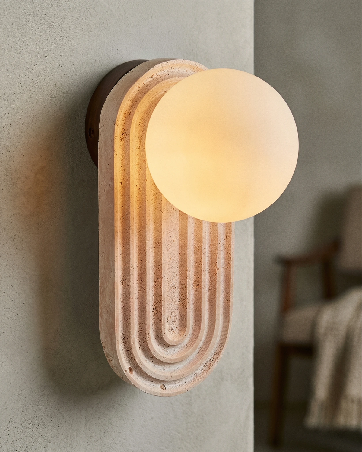 Close-up of the ARCA No.01 travertine wall sconce, fluted arch and lit opal globe seen from an angle