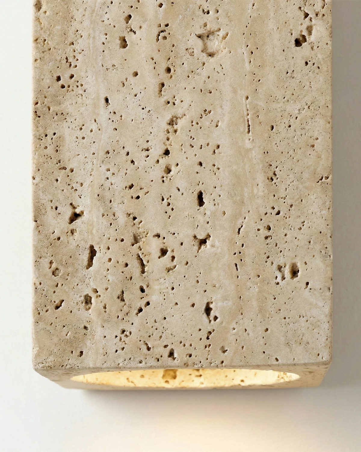 Close-up of the GRANO No.01 travertine wall sconce block with warm light escaping at the bottom edge