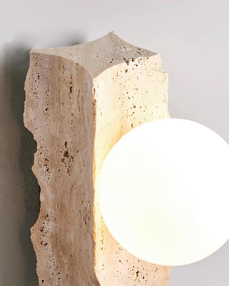 Close-up of the raw travertine slab of the KANSO No.03 wall sconce with the lit opal globe at its lower edge