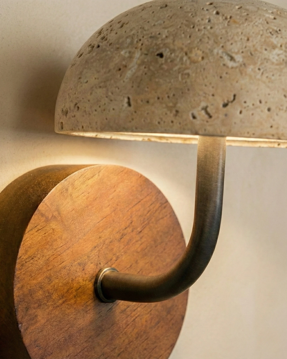 Close-up of the lit travertine dome, black arm and walnut disc of the travertine wall sconce SIENA No.01