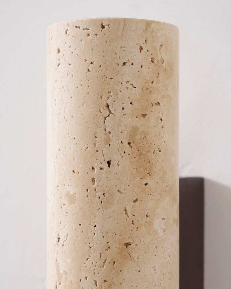 Close-up of the travertine wall sconce STELO No.02 cylinder mounted on a white wall, unlit, walnut bracket below