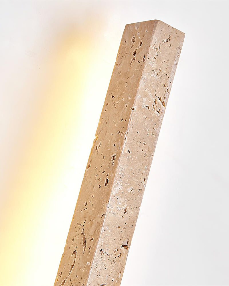 Close-up of the pitted travertine bar of the VITRU No.02 wall sconce with warm light washing the wall behind