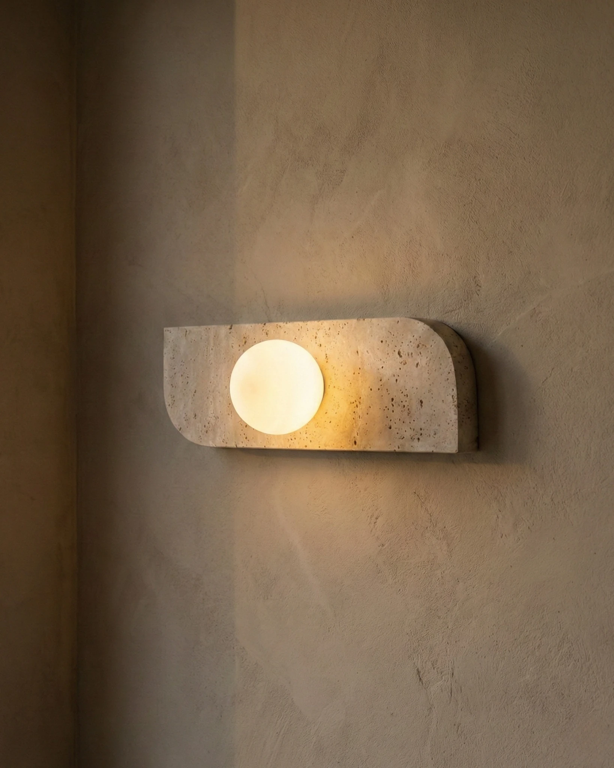 Travertine wall sconce GENOVA No.01 mounted horizontally and lit on a plaster wall