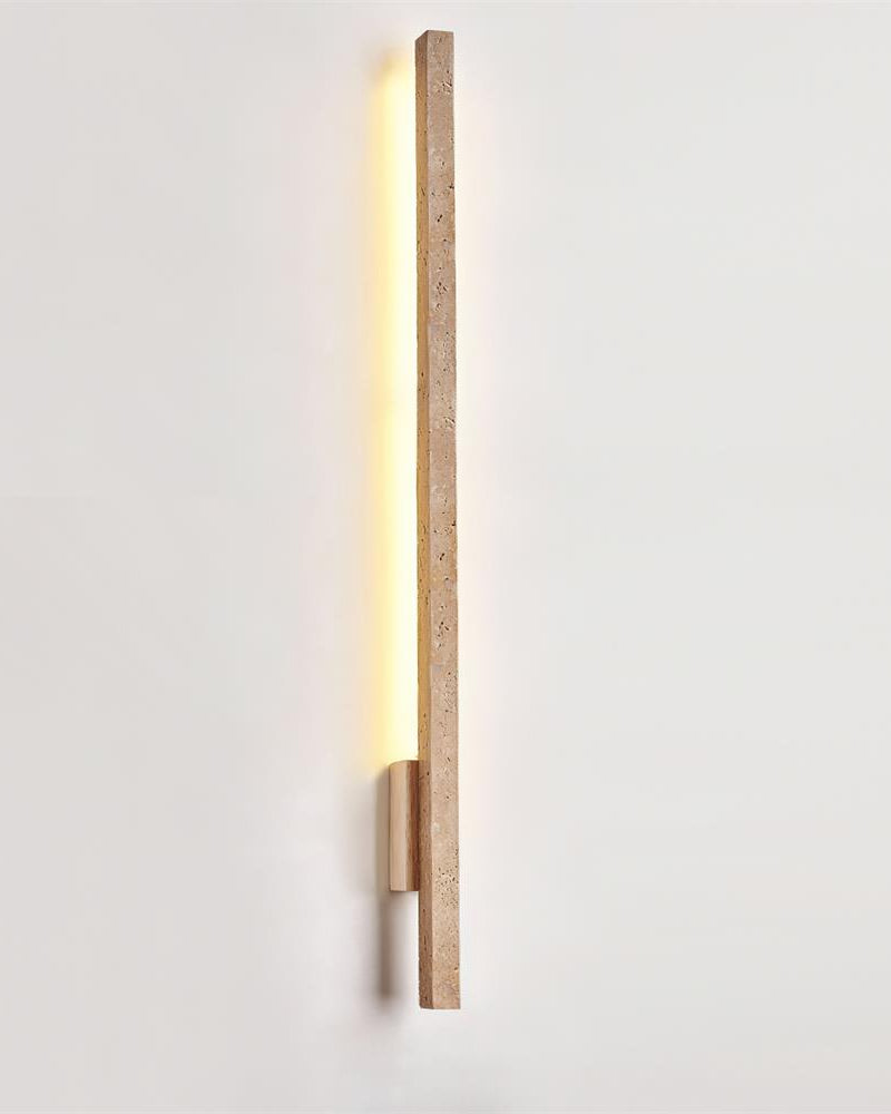 Travertine wall sconce VITRU No.02 Tall in Travertine and Light Wood, slim bar switched on against a white wall
