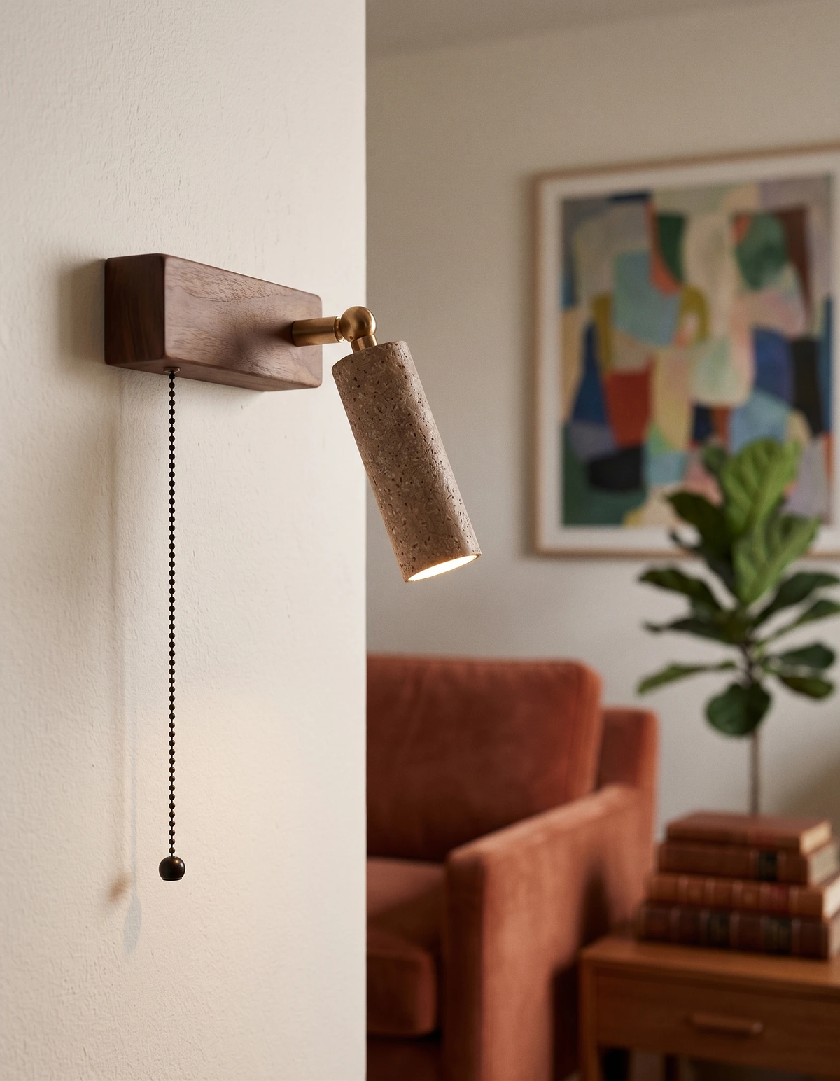 Travertine wall sconce VITRU No.01 in cream travertine, lit on a wall beside colorful art above a rust sofa