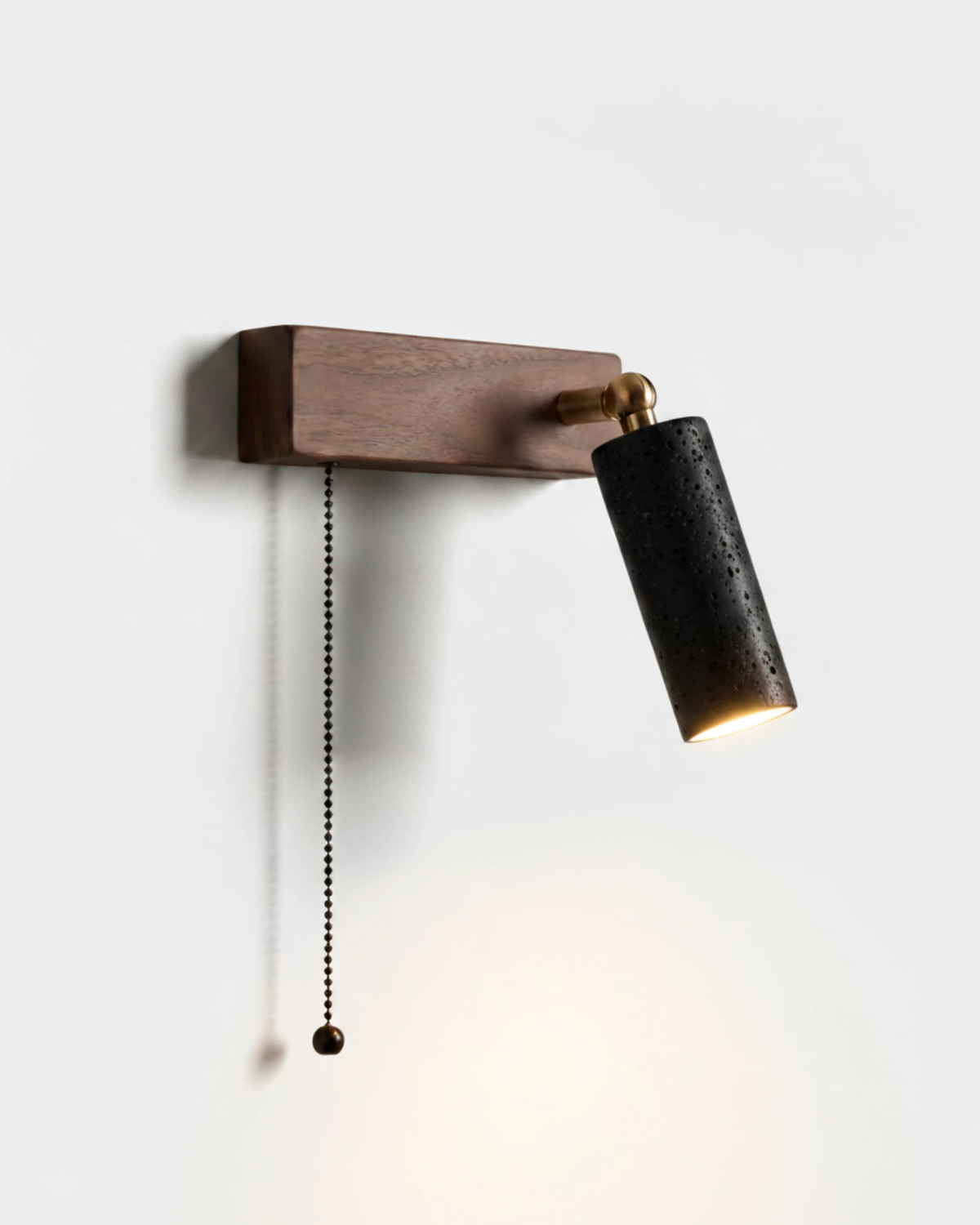 Travertine wall sconce VITRU No.01 in volcano black, black stone cylinder on a walnut block with pull chain, unlit