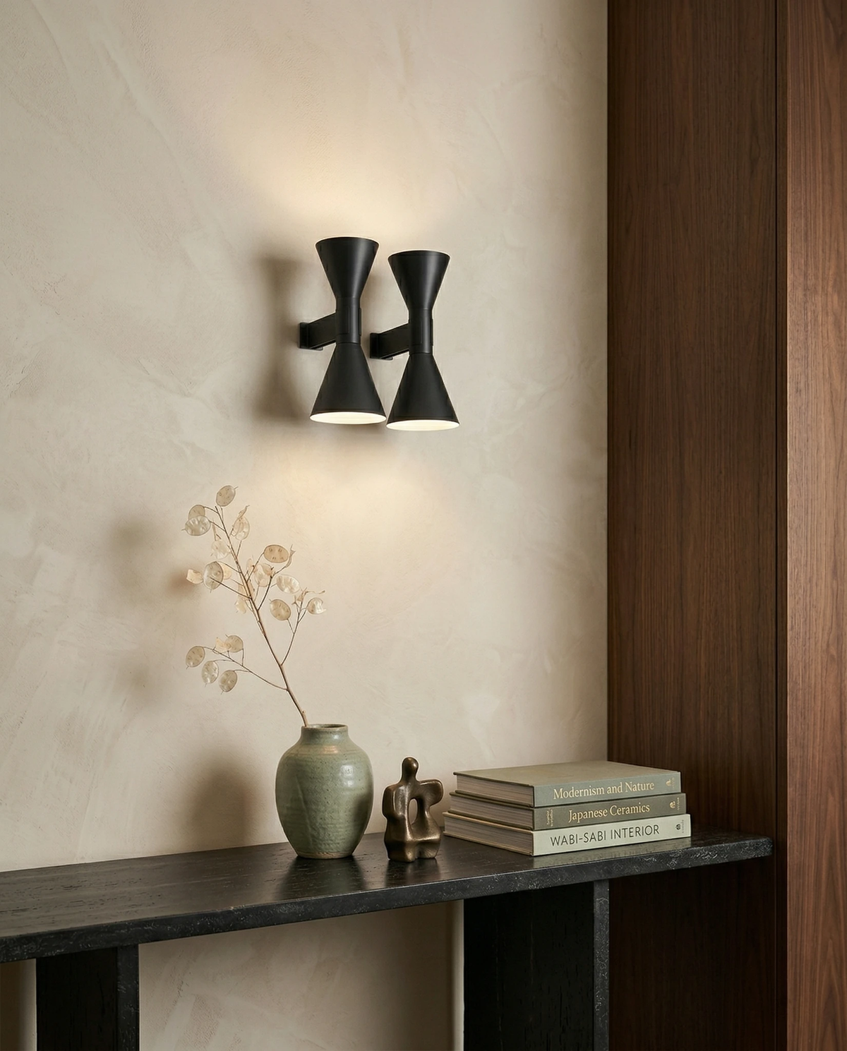 Up down wall sconce ECLISSI No.01, a lit pair in matte black on a plaster wall above a black console with a vase and books
