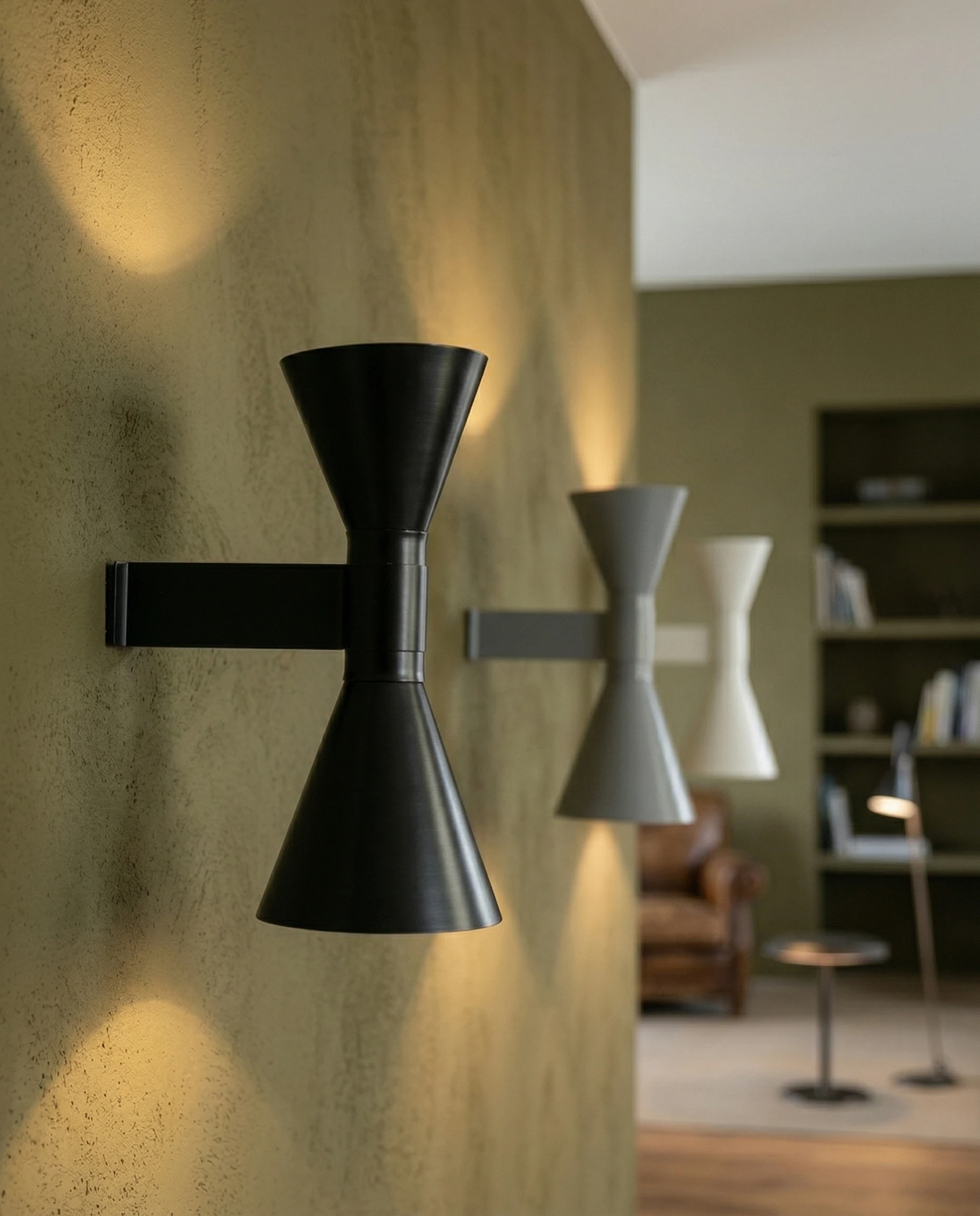 Up down wall sconce ECLISSI No.01 in black, gray and white, three lit units in a row on an olive wall of a living room