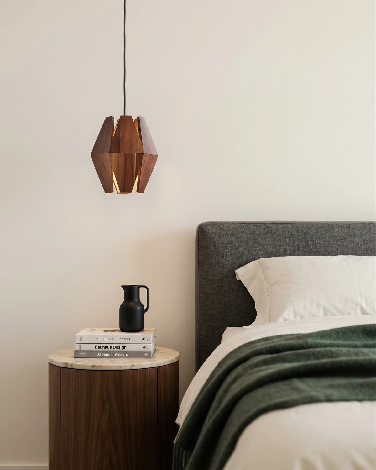 Wood pendant light ORBIT No.01 hanging beside a gray upholstered bed above a round walnut nightstand