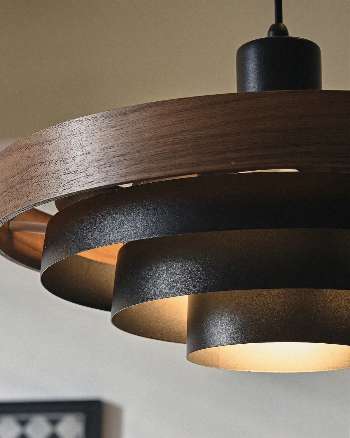 Close-up of the black metal tiers and walnut ring of the STECCA No.01 wood pendant light, lit from within