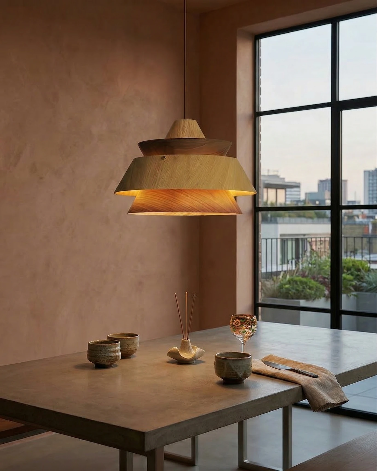 Wood pendant light BOSCO No.01 in light oak lit above a dining table by a window with a city view
