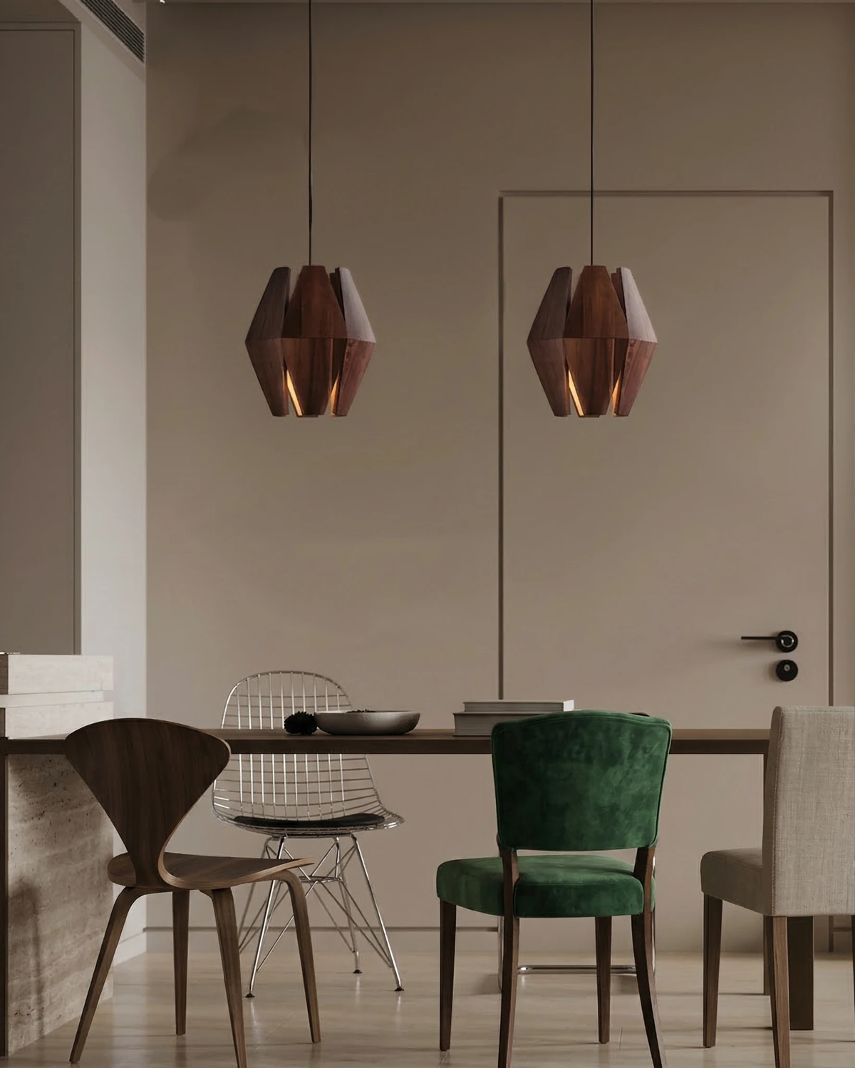 Two wood pendant lights ORBIT No.01 hung over a long dining table with mixed chairs including a green velvet seat