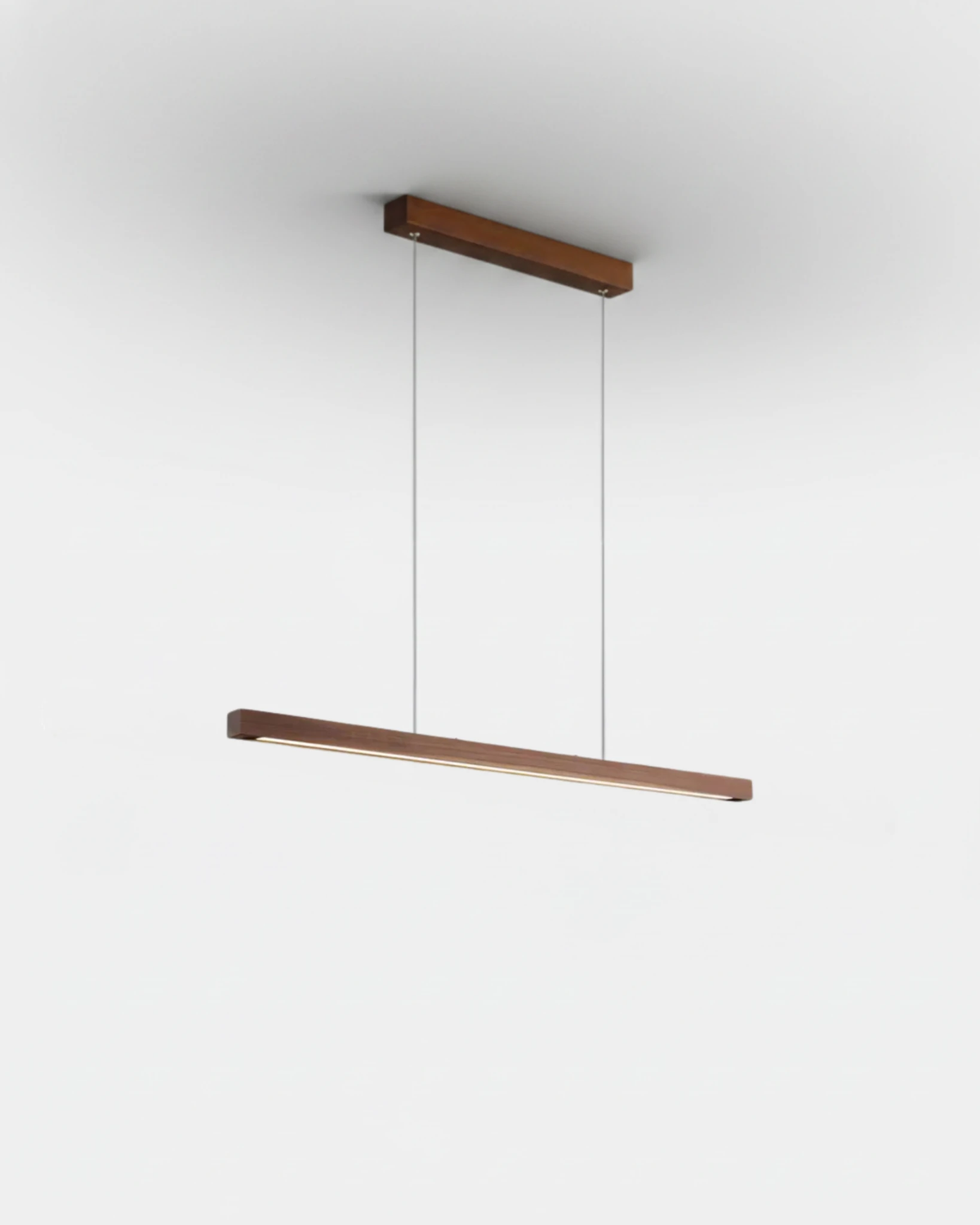 Wood pendant light VIRGA No.01, 31 in walnut brown linear bar hung on thin cables from a matching walnut canopy, lit