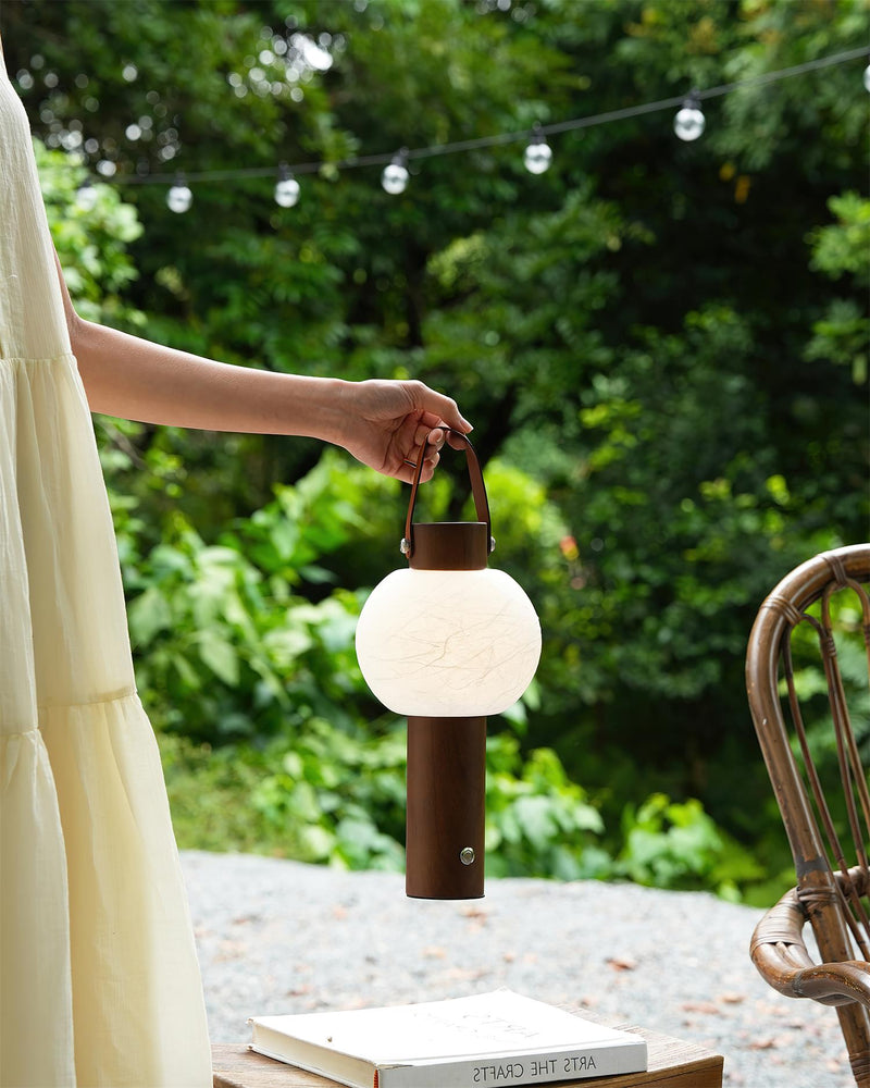 Wood table lamp NAPOLI No.01 carried by its handle in a garden with string lights, globe switched on