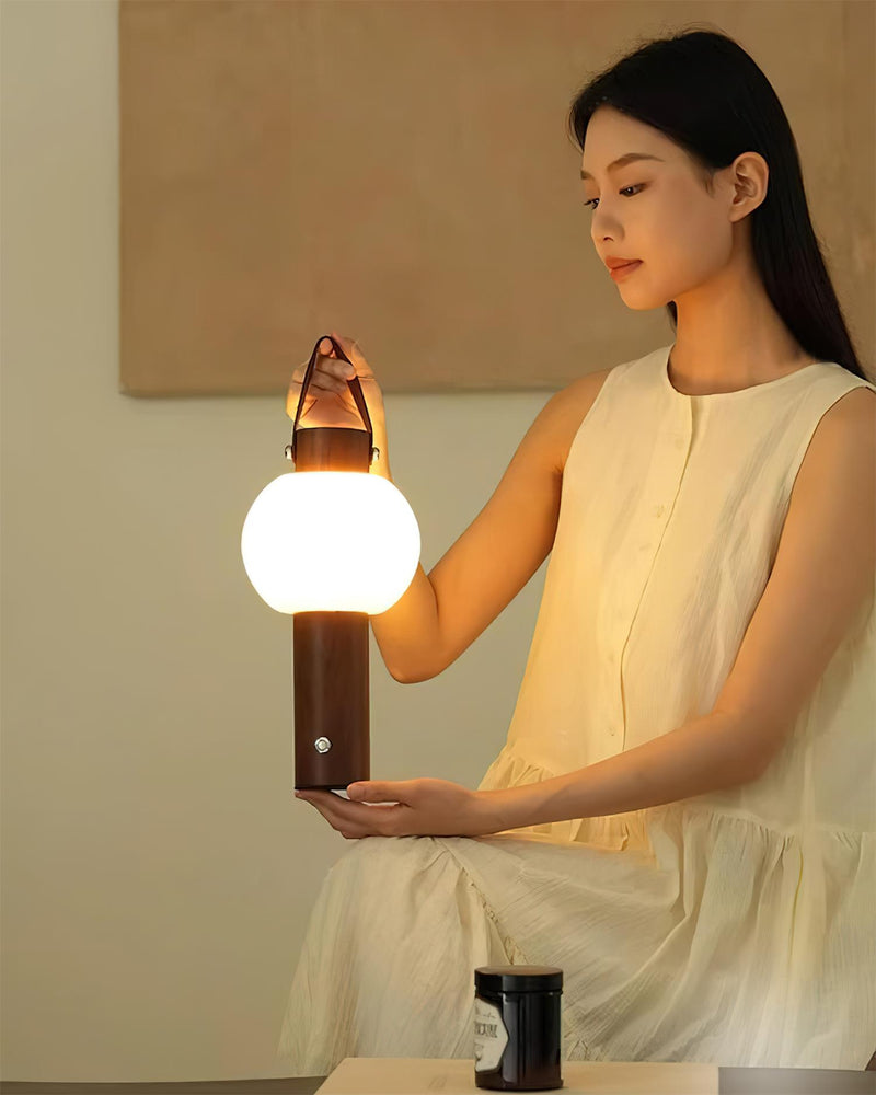 Wood table lamp NAPOLI No.01 lit and held on the lap of a seated woman in a white dress beside a table