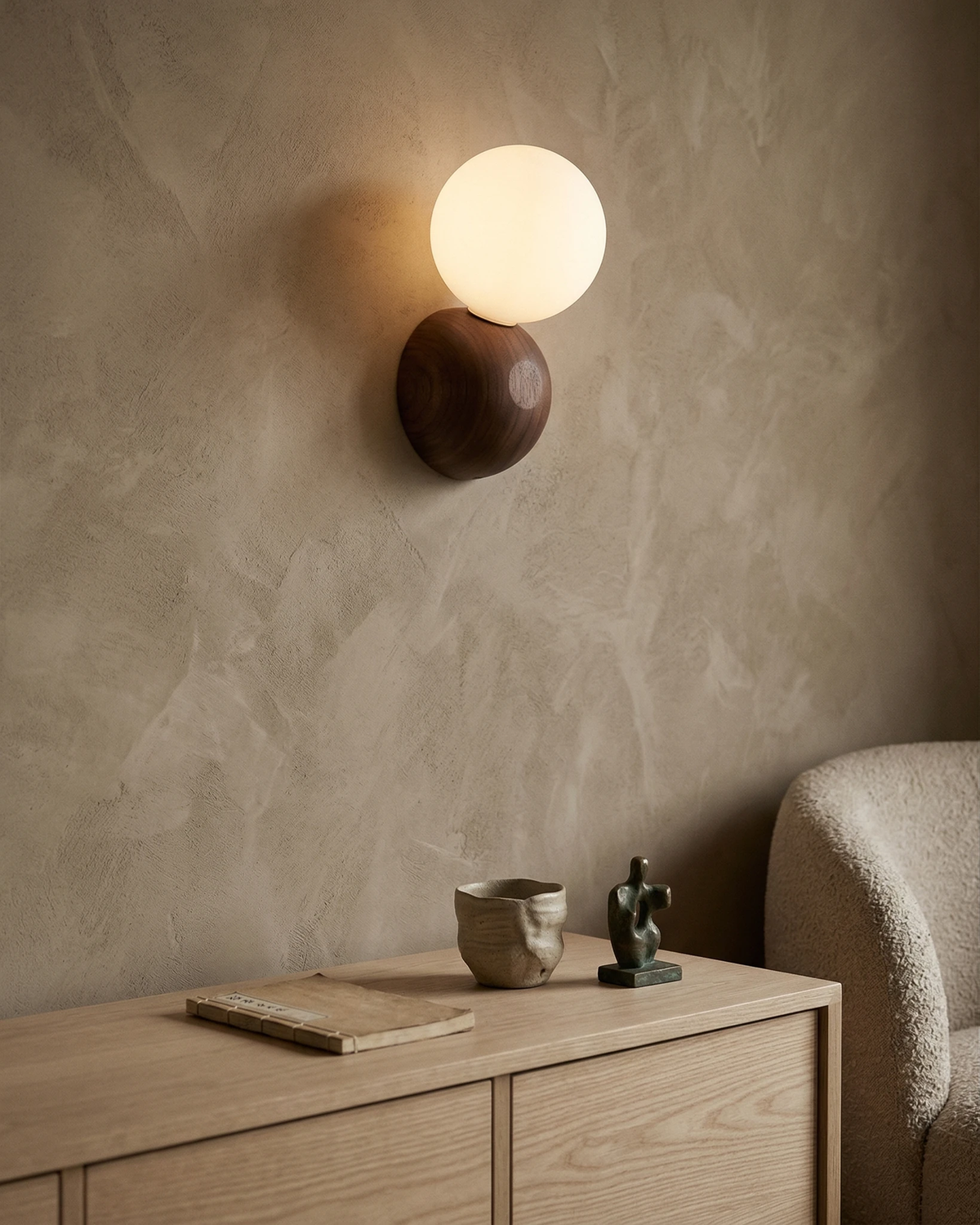Wood wall sconce ALBE No.01 switched on against a beige plaster wall above a light oak sideboard with a mug
