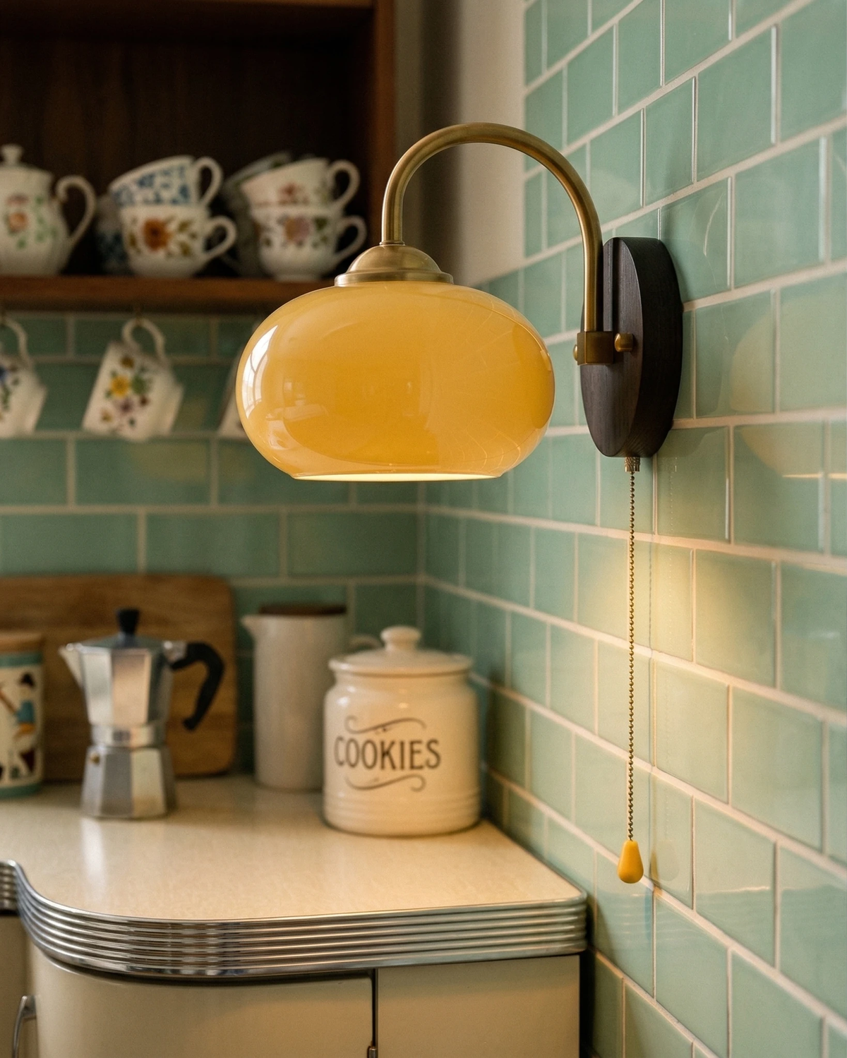 Wood wall sconce CURVA No.02 in soft beige on mint green subway tile above a kitchen shelf of mugs and a cookie jar