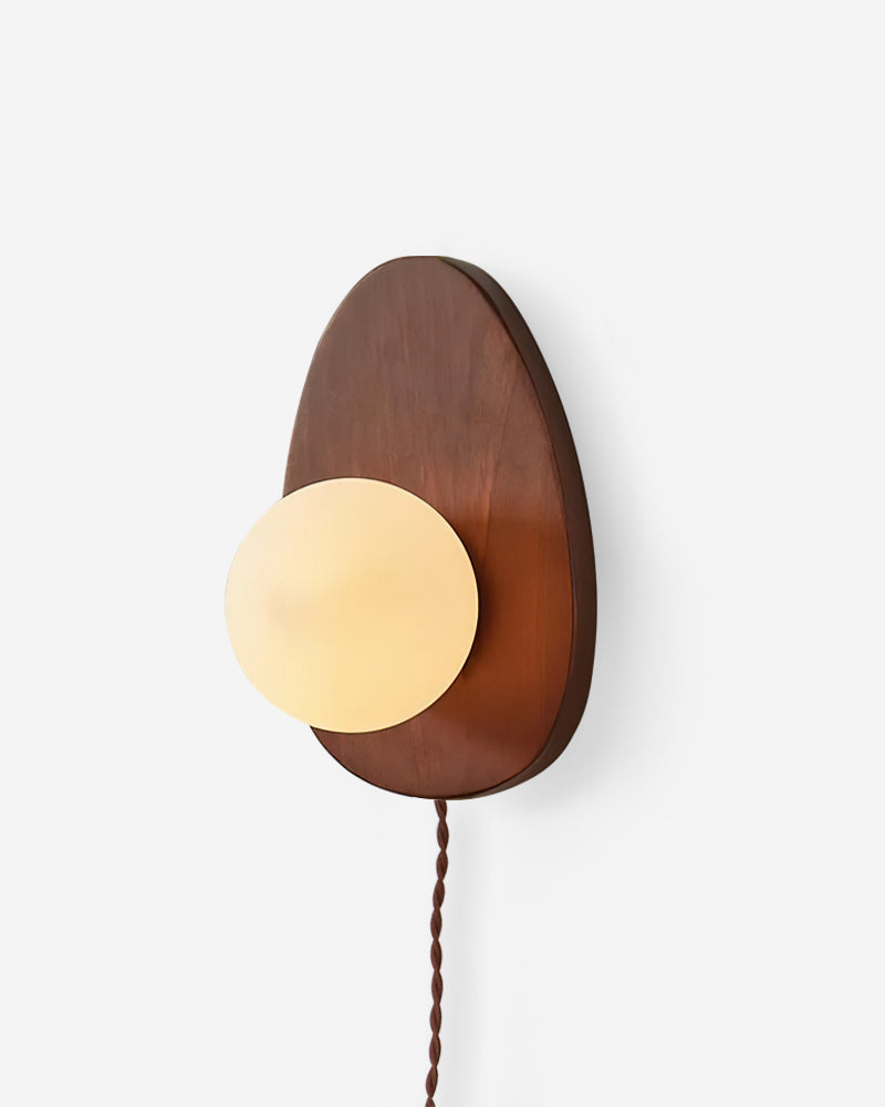 Wood wall sconce FOGLIA No.01 in Dark Walnut, teardrop walnut backplate cradling a glowing opal globe with a cord