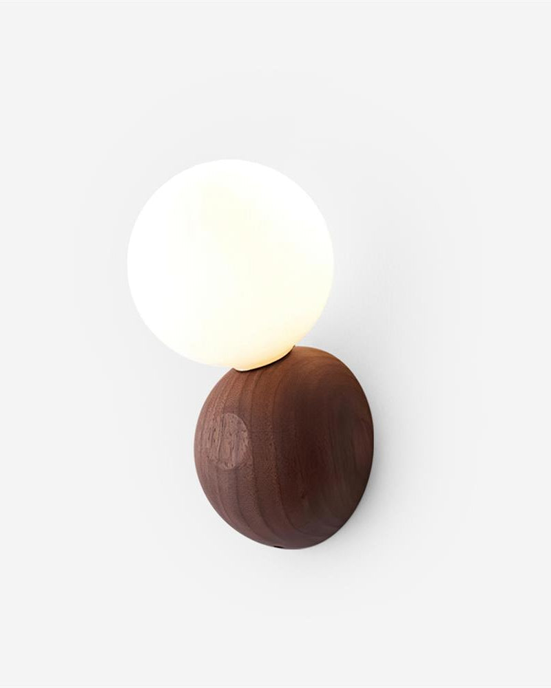Wood wall sconce ALBE No.01 in Walnut on Opal, glowing opal sphere resting on a solid walnut pebble, angled view