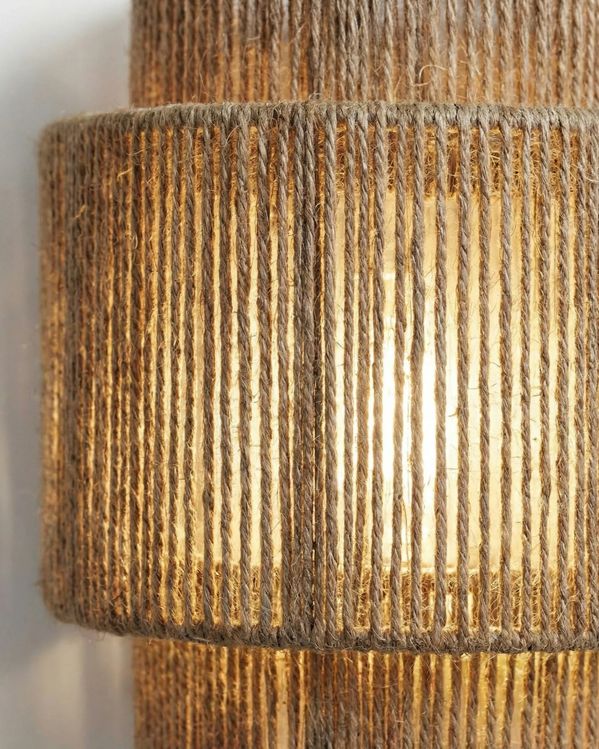 Close-up of the woven wall sconce RAVENNA No.01 showing the vertical jute cords glowing with warm light
